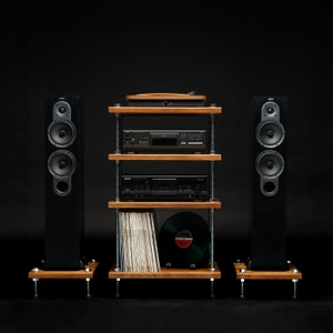 May include: A black stereo system with two speakers, a turntable, a CD player, and a cassette player. The system is on a wooden shelf unit with three shelves. The shelf unit is on a black surface.