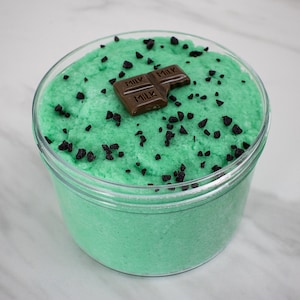 May include: A clear glass jar filled with green slime with black chocolate chips and a small chocolate bar on top that says "Milk" three times.