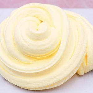 May include: A swirl of pale yellow slime, resembling whipped cream, is displayed against a light-colored surface. The slime has a soft, creamy texture with visible ridges and a smooth, glossy finish. The overall appearance is reminiscent of a dessert.