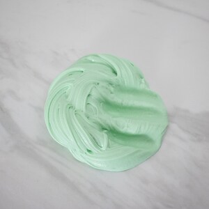 May include: A close-up of a light green slime, a popular sensory toy, on a white marble surface.