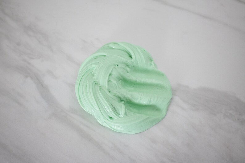 May include: A close-up of a light green slime, a popular sensory toy, on a white marble surface.