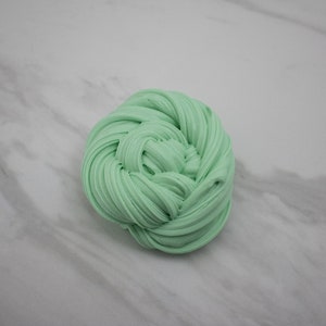 May include: A close-up of a light green slime, rolled into a ball shape. The slime is soft and appears to be very stretchy.