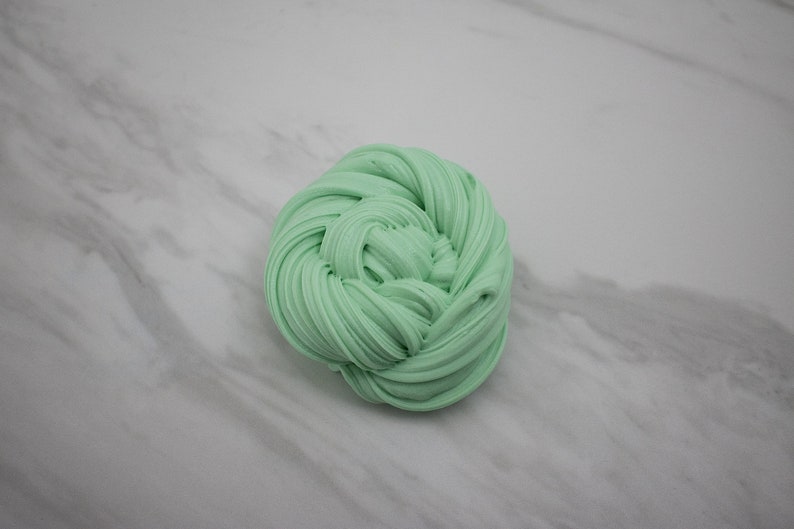 May include: A close-up of a light green slime, rolled into a ball shape. The slime is soft and appears to be very stretchy.