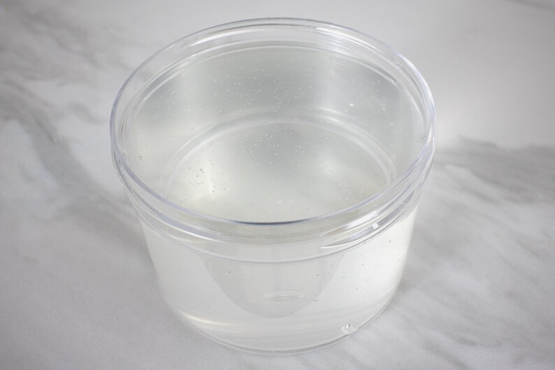 Op de afbeelding: Een doorzichtige plastic container met een deksel, gevuld met een heldere vloeistof.