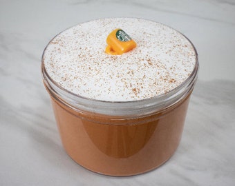 May include: A clear glass jar filled with a light brown liquid topped with a thick layer of white whipped cream and a small green and orange coffee cup charm.