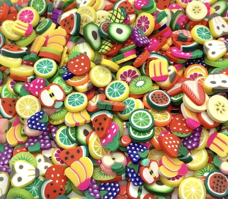 May include: A vibrant assortment of colorful fruit slices, including watermelon, strawberries, lemons, kiwi, and bananas. The miniature fruit shapes are in various sizes and are scattered across the image, creating a playful and cheerful display.
