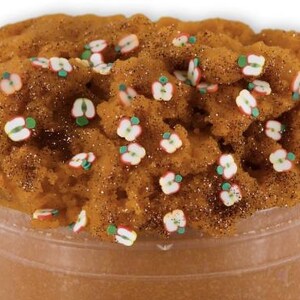 May include: A jar filled with brown, textured slime, sprinkled with glitter and small apple-shaped decorations. The slime has a fluffy appearance and is topped with white, red, and green apple slices.