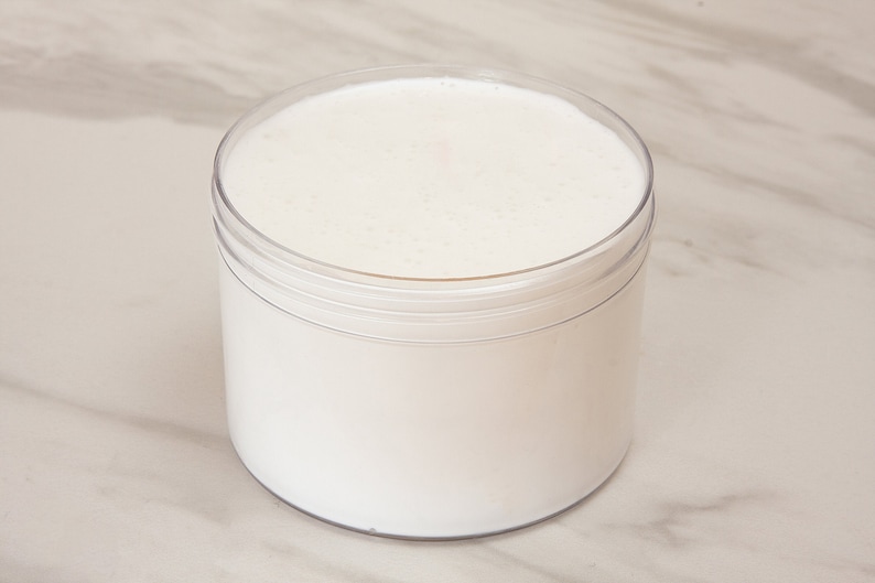 May include: A clear plastic jar filled with a white, creamy substance. The jar is sitting on a white marble surface.