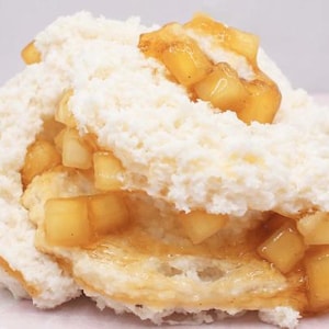 May include: A close-up of a dessert featuring a biscuit base, topped with a generous layer of white, fluffy topping and chunks of golden-brown apples. The apples are glazed with a sweet, syrupy sauce, creating a visually appealing treat.