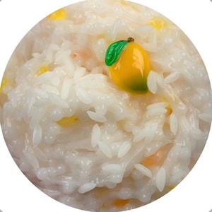 May include: A close-up of a white rice slime with a yellow and green mango charm on top.