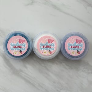 May include: Three small containers of slime, each with a pink and white label that says "Andrea's Slime Boutique". The slime is blue, white, and sparkly.