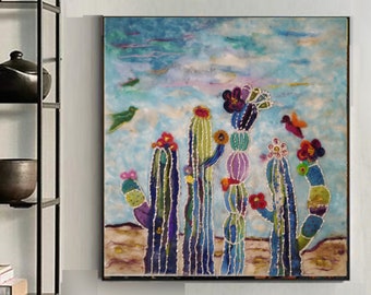 Op de afbeelding: Een kleurrijk abstract schilderij van cactussen met bloemen en een vogel in een woestijnlandschap. Het schilderij is ingelijst en hangt aan een witte muur. De tekst "Keche Fine Art" is zichtbaar onder het schilderij.
