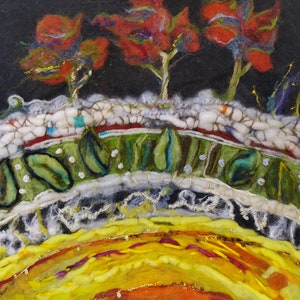 Op de afbeelding: Een close-up van een viltkunstwerk dat een zonsondergang over een landschap voorstelt. De lucht is diep zwart met rode, oranje en gele bomen. De voorgrond is een groen veld met witte en groene bladeren. De zon is helder geel en oranje.