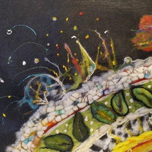 Op de afbeelding: Een close-up van een kleurrijk viltkunstwerk met een textuur. Het kunstwerk heeft een verscheidenheid aan kleuren, waaronder wit, zwart, groen, rood en geel. Het kunstwerk is gemaakt van kleine stukjes vilt die aan elkaar zijn genaaid om een uniek ontwerp te cre&euml;ren.