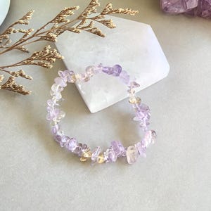 Può includere: Un braccialetto delicato realizzato con piccoli frammenti irregolari di cristalli di ametista e citrino. Il braccialetto è di colore viola chiaro e giallo.
