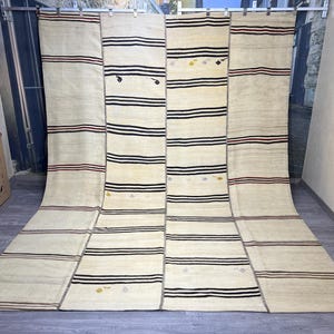 May include: A white, cream, and black striped rug with a woven design. The rug is made up of six panels, each with a different pattern.