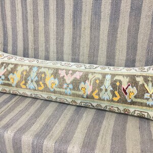 May include: A long, rectangular pillow with a light green background and a colorful geometric pattern. The pattern features a repeating design of stylized flowers and leaves in shades of pink, blue, yellow, and brown.