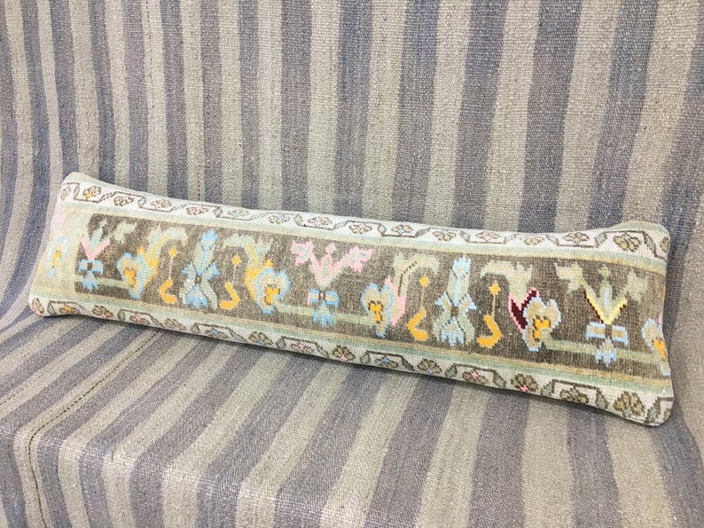 May include: A long, rectangular pillow with a light green background and a colorful geometric pattern. The pattern features a repeating design of stylized flowers and leaves in shades of pink, blue, yellow, and brown.