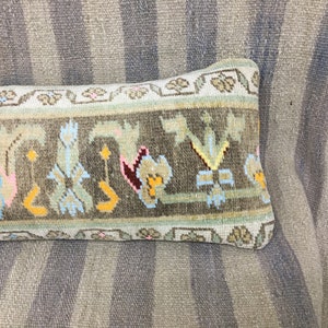 May include: A long, rectangular pillow with a brown, green, and white patterned fabric. The pillow has a floral design with pink, yellow, and blue accents.