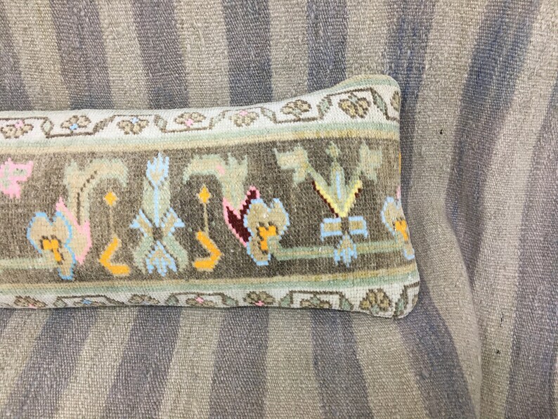 May include: A long, rectangular pillow with a brown, green, and white patterned fabric. The pillow has a floral design with pink, yellow, and blue accents.
