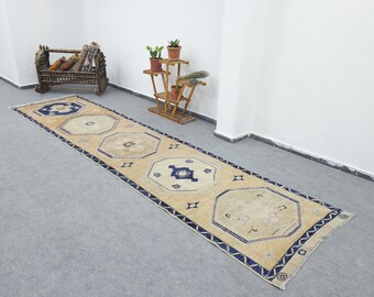 May include: A long, rectangular rug with a beige background and geometric patterns in navy blue. The rug features a central design of octagonal shapes and a border with a repeating pattern. The rug is placed on a gray floor.