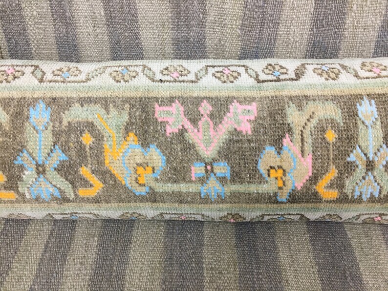 May include: Close-up of a brown and beige patterned rug with a floral design. The rug has a fringe border and is made of wool.