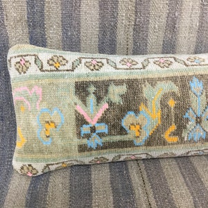 May include: A long, rectangular pillow with a floral pattern in shades of blue, pink, yellow, and brown. The pillow is made of a woven fabric and has a fringed edge.
