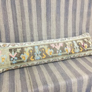 May include: A long, rectangular pillow with a light blue background and a colorful floral pattern. The pillow is made of woven fabric and has a fringe border.