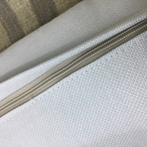 May include: Close-up of a light gray pillow with a zipper running along the edge. The pillow has a subtle textured pattern.