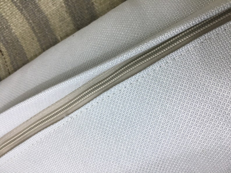 May include: Close-up of a light gray pillow with a zipper running along the edge. The pillow has a subtle textured pattern.