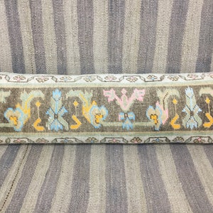 May include: A long, rectangular pillow with a light blue background and a brown, green, pink, and yellow geometric pattern. The pillow is made of woven fabric and has a fringe border.