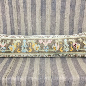 May include: A long, rectangular pillow with a light blue background and a brown, green, and yellow floral pattern. The pillow is made of a soft, woven fabric and has a fringed edge.