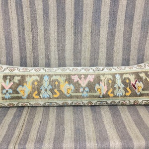 May include: A long, rectangular pillow with a brown background and a colorful floral pattern. The pillow is made of woven fabric and has a fringed edge.