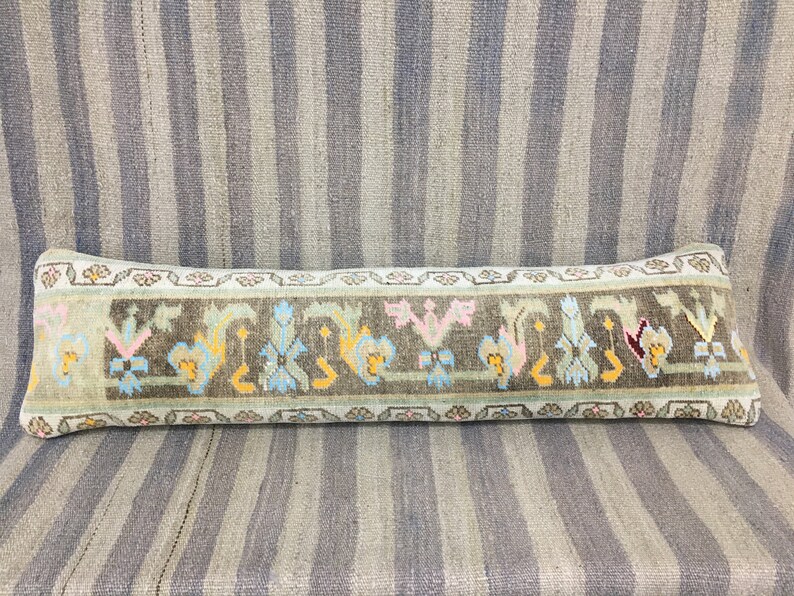 May include: A long, rectangular pillow with a brown background and a colorful floral pattern. The pillow is made of woven fabric and has a fringed edge.