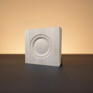 May include: A light wood block with a circular design carved into the front. The block is smooth and has a natural wood grain.