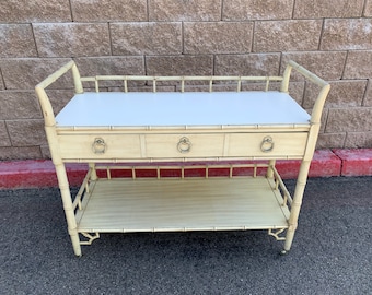 May include: A white bamboo serving cart with two shelves and a single drawer. The cart has a white top and brass hardware.