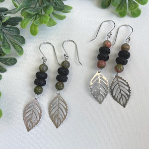 May include: Two pairs of dangle earrings featuring silver-toned metal hooks, each with a vertical arrangement of two round green beads, two textured black lava beads, and a single round green bead, finished with a silver-toned metal leaf charm.