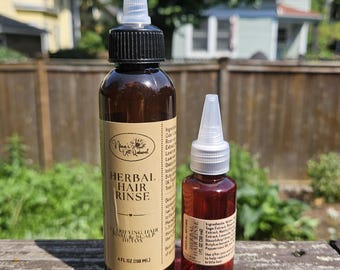 May include: Two amber plastic bottles of Nina's All Natural Herbal Hair Rinse with black and white twist-top caps. The larger bottle is 4 fl oz (118 ml) and the smaller bottle is 1 fl oz (30 ml). Both feature tan labels with black text.