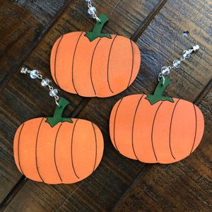 May include: Three orange pumpkin ornaments with green stems and black lines. Each pumpkin has a clear beaded string attached to the top.