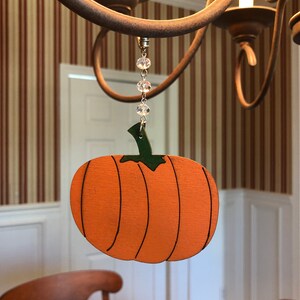 May include: A wooden pumpkin ornament with a green stem and orange paint hangs from a chandelier with a crystal bead chain.