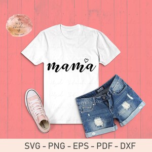 Pu&ograve; includere: Maglietta bianca con la parola "mama" in lettere corsive nere e un piccolo cuore sopra la "a". La maglietta &egrave; appoggiata su uno sfondo rosa con un paio di pantaloncini di jeans blu e una scarpa da ginnastica rosa.