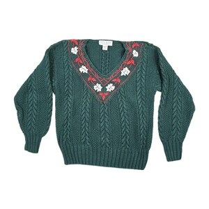 May include: A dark green sweater with a V-neck and long sleeves. The neckline is decorated with white floral embroidery and red accents. The sweater has a cable knit design.