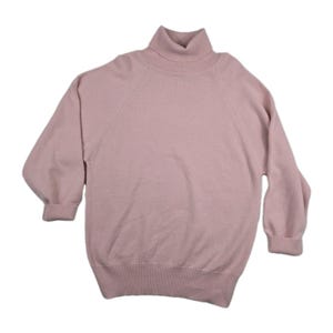 May include: A light pink turtleneck sweater with long sleeves. The sweater has a ribbed hem and cuffs, and a classic turtleneck collar. The sleeves are a three-quarter length. The sweater is made of a soft, knitted material.