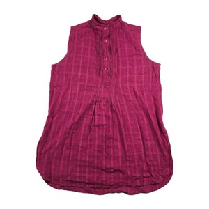 May include: A sleeveless, magenta-colored blouse with a mandarin collar and a button-down placket. The fabric has a subtle plaid pattern. The blouse has pleats on the front and a rounded hemline. This top is suitable for casual or semi-formal wear.