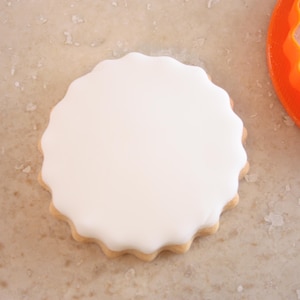 A white, round cookie cutter is placed on a speckled surface next to an orange cookie cutter.