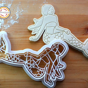 Può includere: Due stampini per biscotti in plastica bianca a forma di sirene. Lo stampino a sinistra presenta un design dettagliato con squame e una coda fluida. Lo stampino a destra è un design più semplice con una lunga coda fluida.