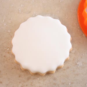 A white, round cookie cutter is placed on a speckled surface next to an orange cookie cutter.