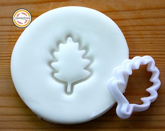 Puede incluir: Cortador de galletas de plástico blanco en forma de hoja de roble. El cortador se muestra junto a un molde de plástico blanco con el mismo diseño de hoja.