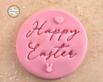 May include: Pink fondant cookie cutter with the text "Happy Easter" in cursive script. The cutter also features a small heart and a bunny rabbit.