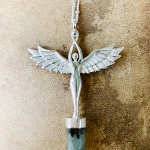 Pode incluir: Colar de prata com um pingente que apresenta uma figura de anjo detalhada com asas e uma pedra preciosa cinza na parte inferior.